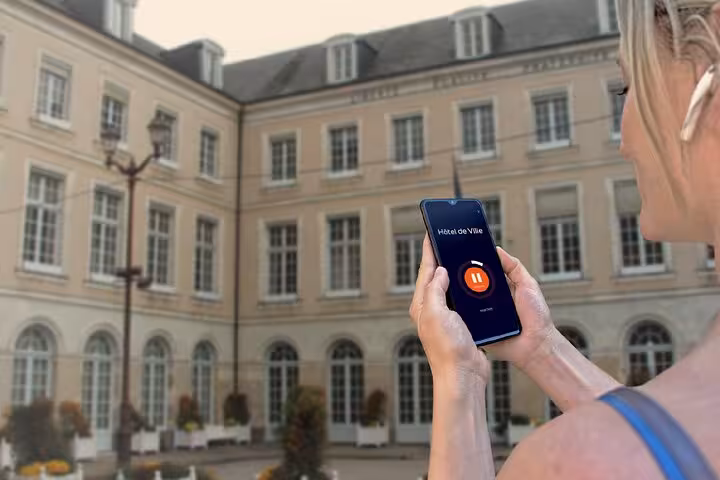 Tourist holding smartphone with audio guide app in front of Le Mans Hôtel de Ville