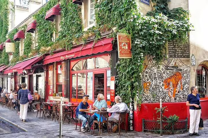 Outdoor café terrace with ivy-covered walls and red awnings in Le Marais, Paris