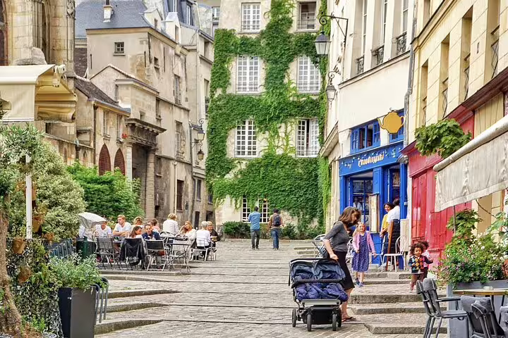 Charming cobblestone street in Le Marais Paris with ivy-covered buildings, outdoor cafés, and strolling visitors