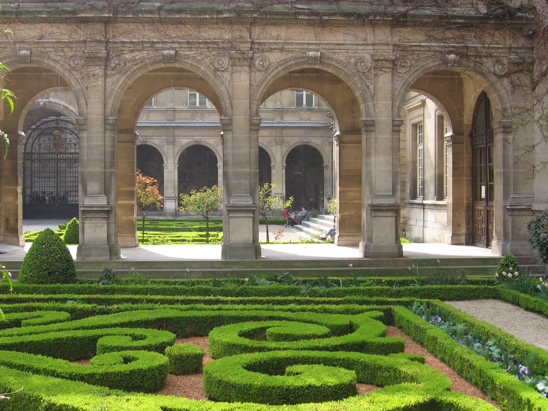 Ornate stone archways and manicured French formal garden at a historic Marais mansion in Paris