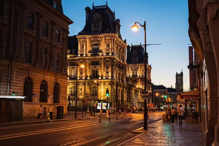 Illuminated Hôtel de Ville at dusk in Le Marais district, Paris, with glowing street lamps and busy sidewalks