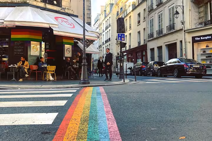 Rainbow crosswalk at a Parisian street corner in Le Marais with café terrace and classic Haussmann buildings