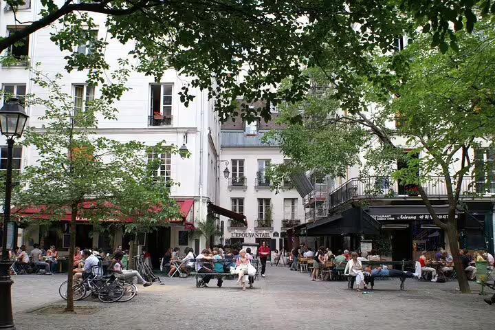 Charming Parisian square in Le Marais with outdoor café terraces, lush trees, and locals relaxing on benches