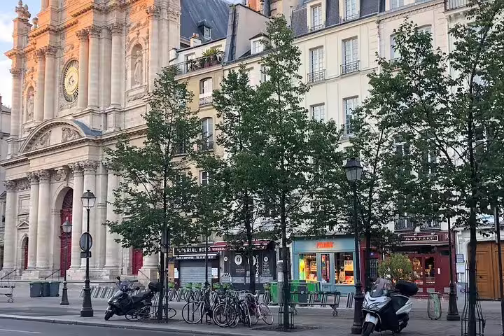 Le Marais neighborhood street with classic Parisian church facade, trees, bikes, and shops in Paris