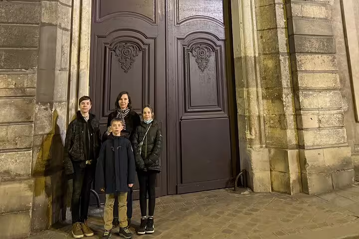 Family of four posing at night in front of ornate wooden doors in Le Marais, Paris
