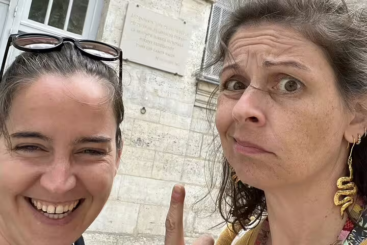 Two women taking a selfie in front of a historic stone building plaque in Le Marais, Paris