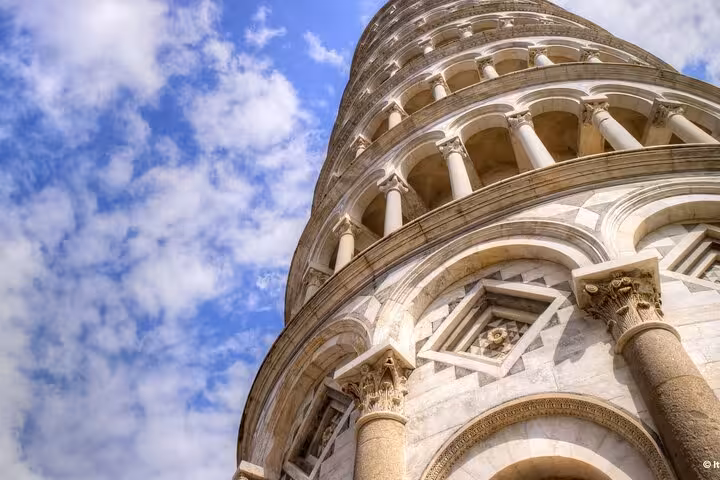 Close-up of the Leaning Tower of Pisa's intricate architecture under a vibrant blue sky, part of a Florence day tour.