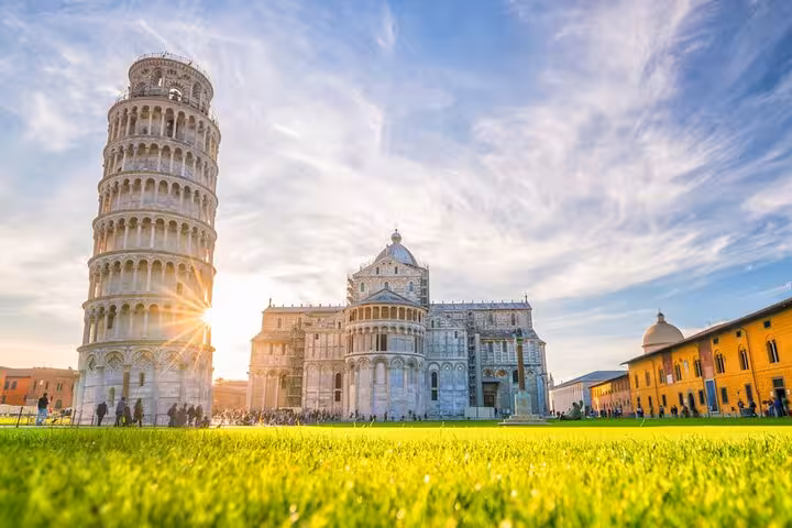 The Leaning Tower of Pisa and Pisa Cathedral bathed in golden sunlight against a vibrant green lawn, perfect for day trips.