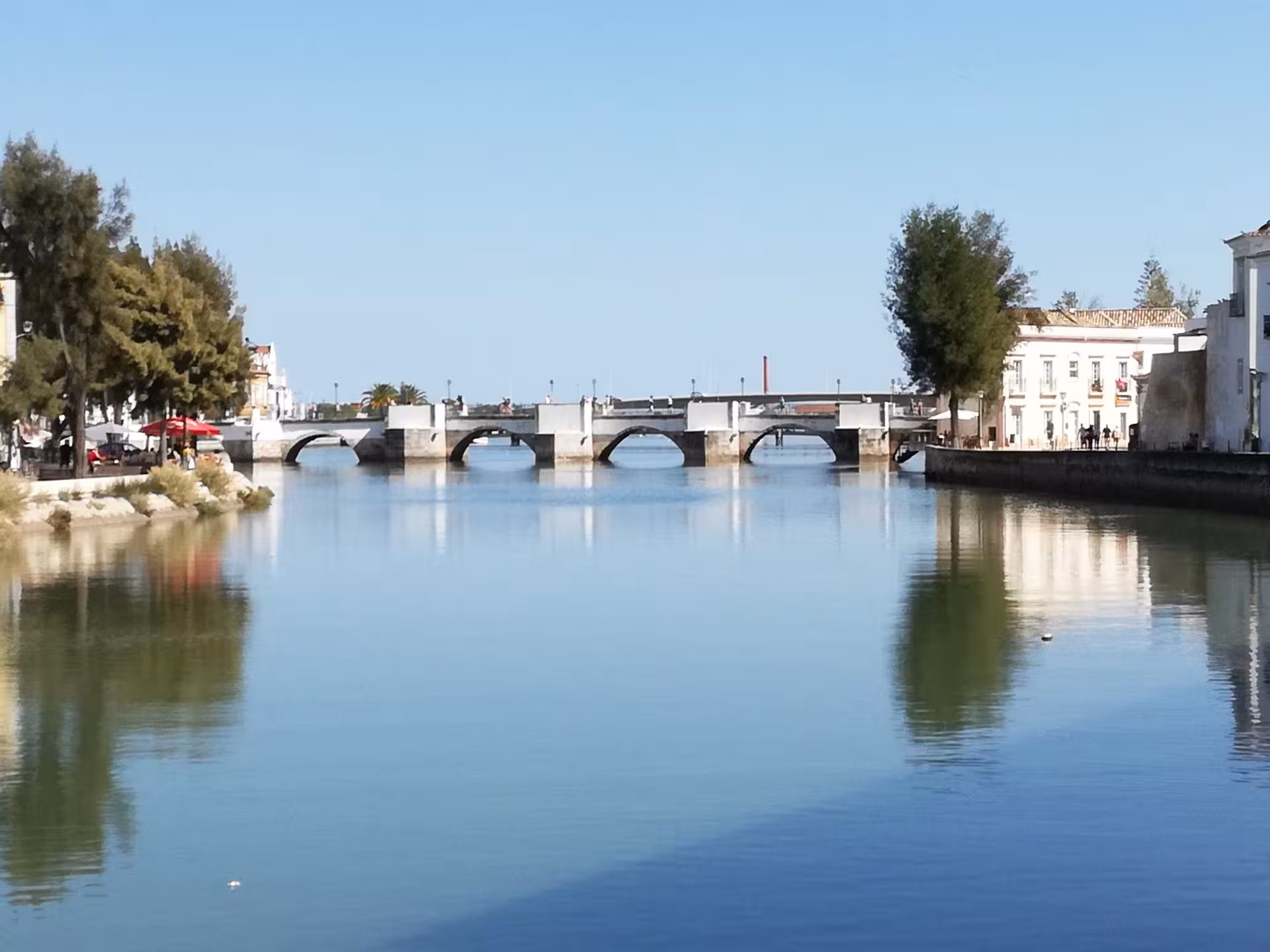 Sunlit stone bridge over calm river in Tavira, Algarve, Portugal, a scenic stop on The Secrets of the Leeward Islands tour