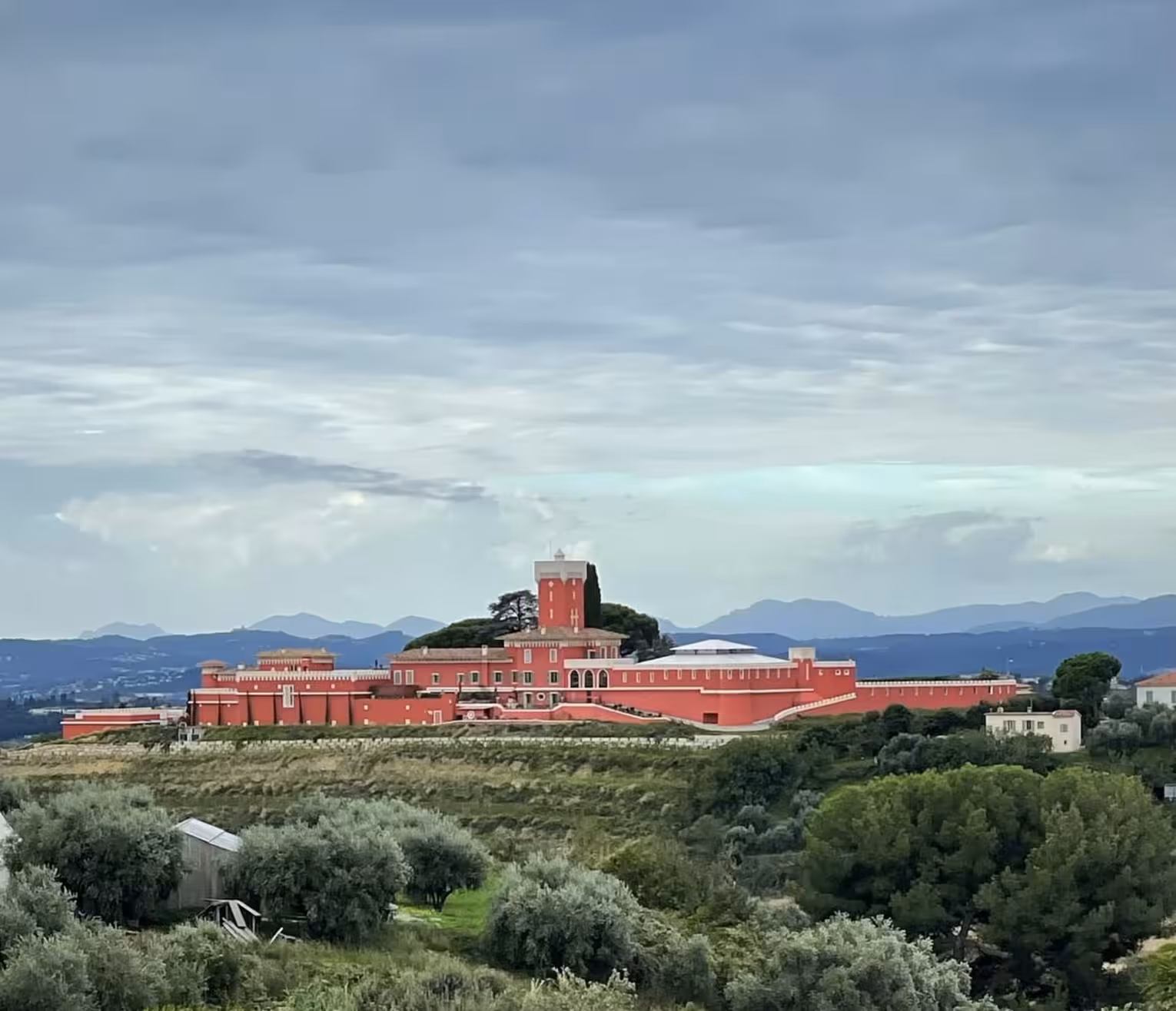 Red hilltop vineyard estate with tower surrounded by olive trees and mountains near Nice