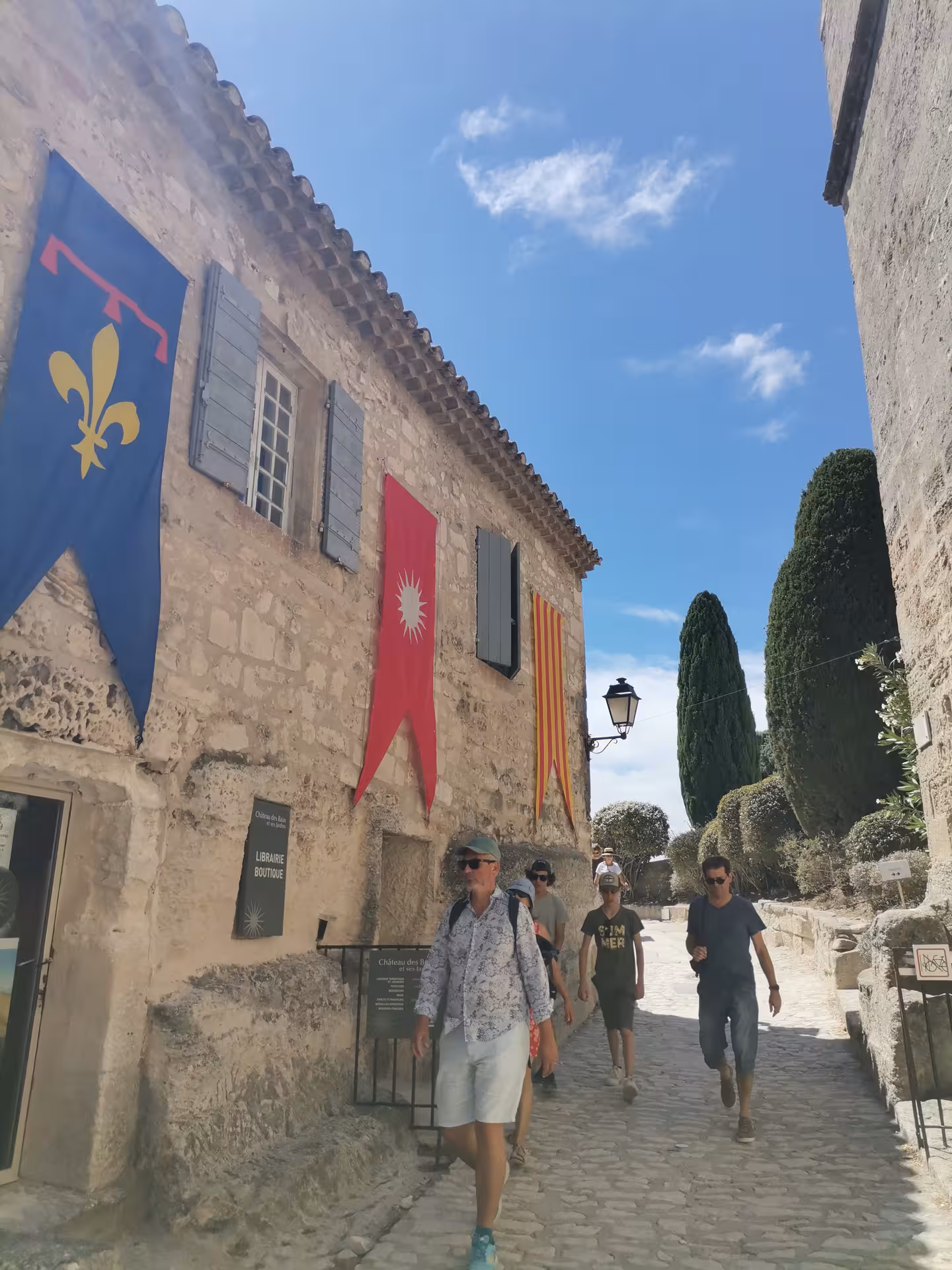 Walking tour in Les Baux-de-Provence medieval village street with stone houses and banners on Arles day trip