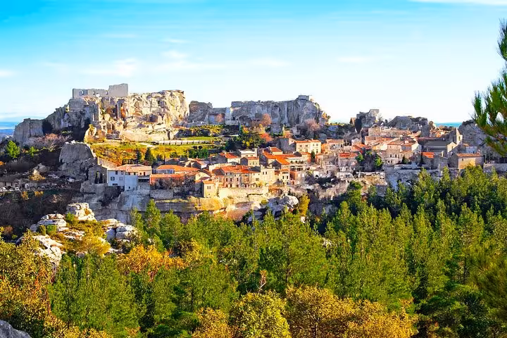 Scenic view of Les Baux de Provence village with historic stone buildings and lush greenery under a bright blue sky.