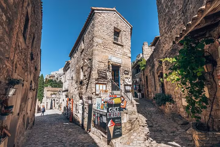 Picturesque narrow street in Les Baux de Provence, featuring historic stone buildings and a quaint café.