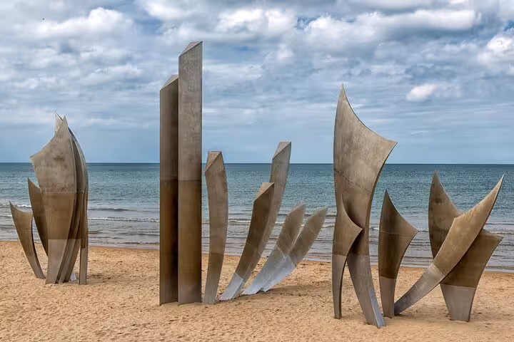 Les Braves sculpture on Omaha Beach, Normandy, with metallic wing-shaped monuments on sandy shore