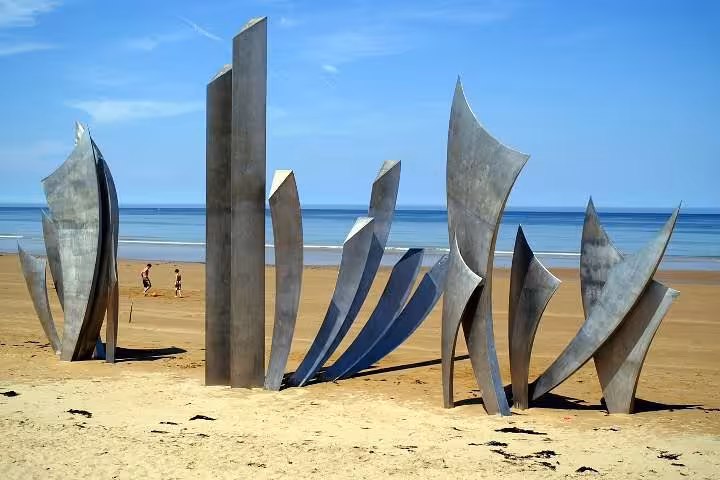 Les Braves sculpture on Omaha Beach, Normandy, with sandy shore and blue sea in background