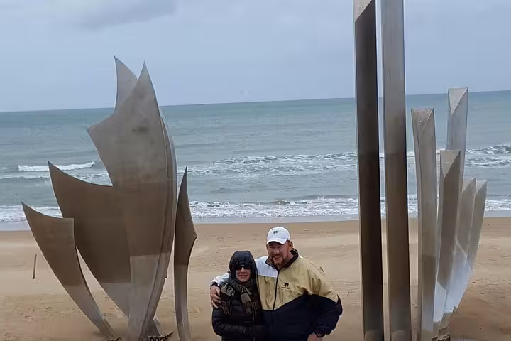 Couple posing at Les Braves sculpture on Omaha Beach, Normandy, on a cloudy day