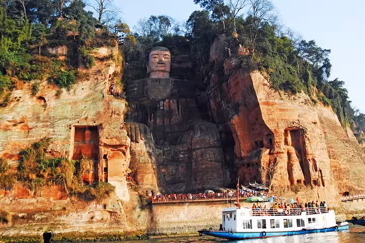 Majestic Leshan Giant Buddha carved into a cliffside with a boat tour in the foreground, showcasing Sichuan's cultural heritage.