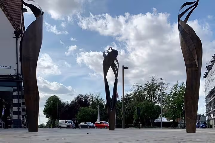 Three tall abstract bronze sculptures in Letchworth Garden City town square under a cloudy sky