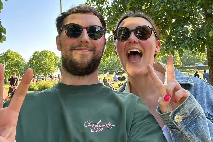 Two smiling visitors in sunglasses giving peace signs in a sunny park during a walking tour