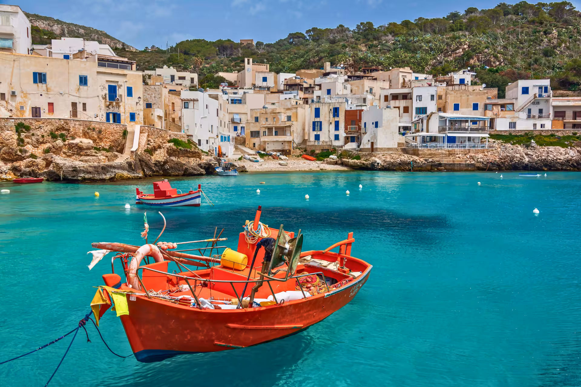 Levanzo fishing village harbor with red boat and turquoise water, stop on Egadi Islands boat tour from Trapani
