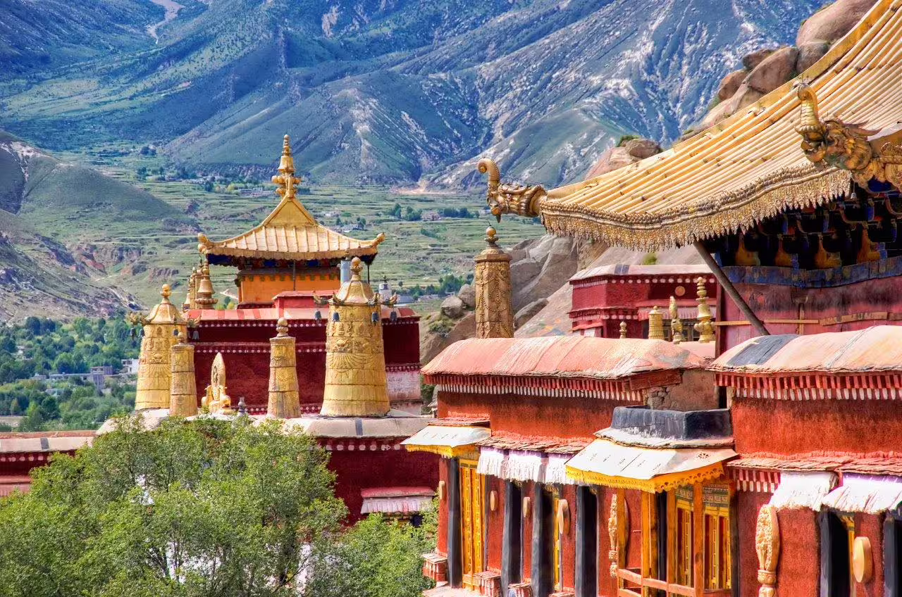 Scenic view of vibrant Tibetan monastery roofs amidst lush green mountains on Lhasa cultural tour.