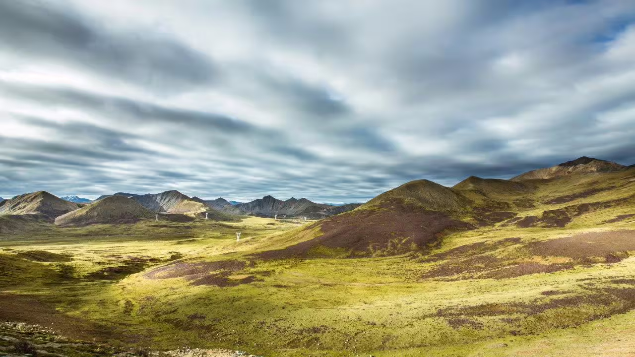 Vast Tibetan plateau landscape under dramatic skies, showcasing rolling hills and distant mountains near Lhasa.