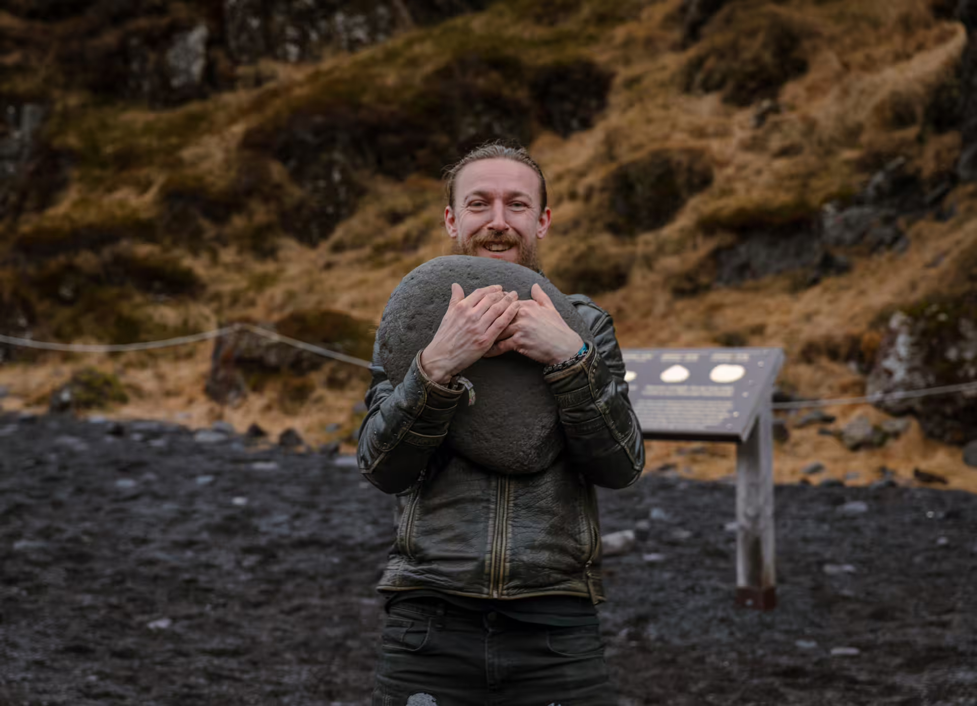 Smiling man holding large round lifting stone on black volcanic beach at Snaefellsnes Peninsula