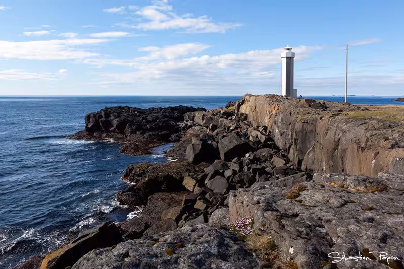 Rocky coastal cliffs with a lighthouse overlooking the blue sea in East Iceland