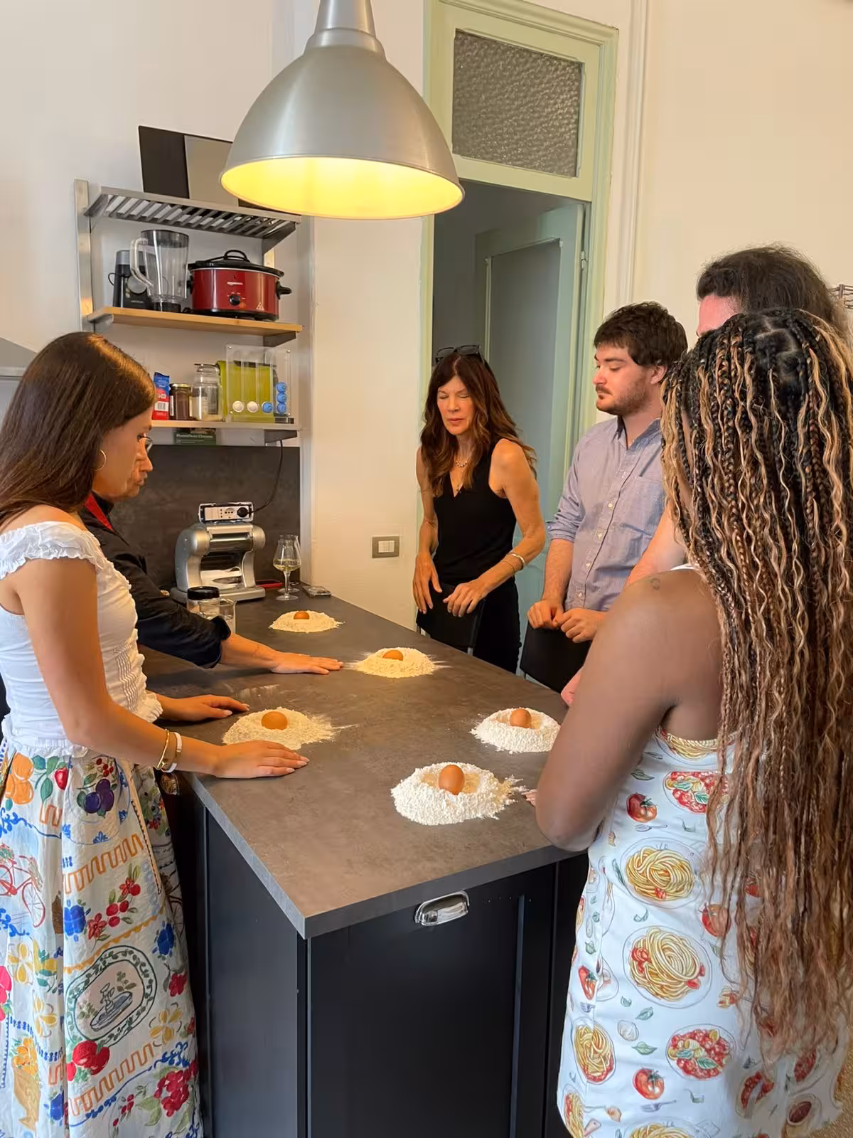 Participants in a Ligurian cooking class learning to make pasta dough in a bright, modern kitchen.