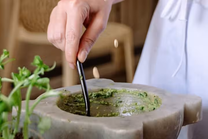 A hand skillfully mixes fresh pesto in a traditional mortar, highlighting Ligurian culinary techniques near Portofino.