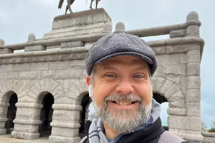 Smiling man with beard and flat cap selfie at historic stone monument in Lincoln Park Chicago