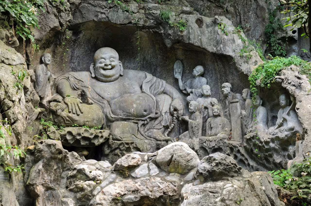 Intricate stone carvings of a laughing Buddha and disciples at Hangzhou's Lingyin Temple.