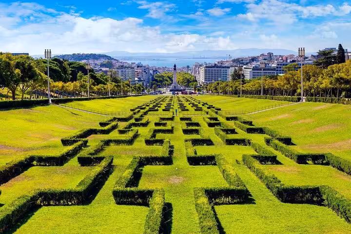 Aerial view of Eduardo VII Park's geometric hedges leading to Lisbon cityscape and Tagus River.