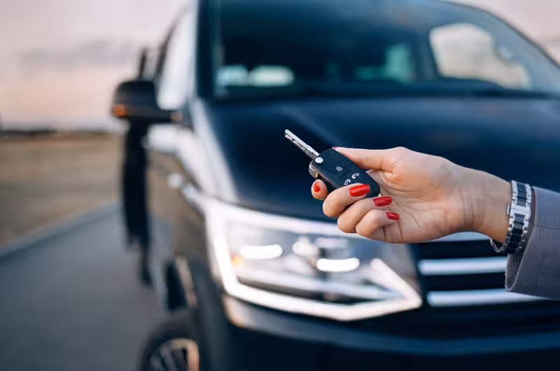 Hand holding car key in front of luxury van for private Lisbon airport to hotel transfer service.