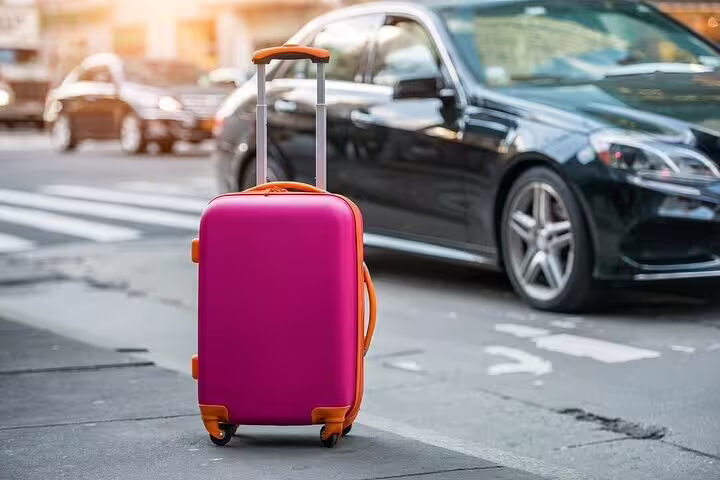 Vibrant pink suitcase beside luxury car highlights private transfer service from Lisbon Metropolitan Area to airport.