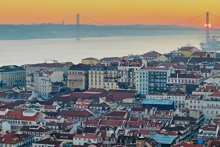 A stunning sunrise view over Lisbon's city center with the iconic bridge in the background, ideal for airport transfer listings.
