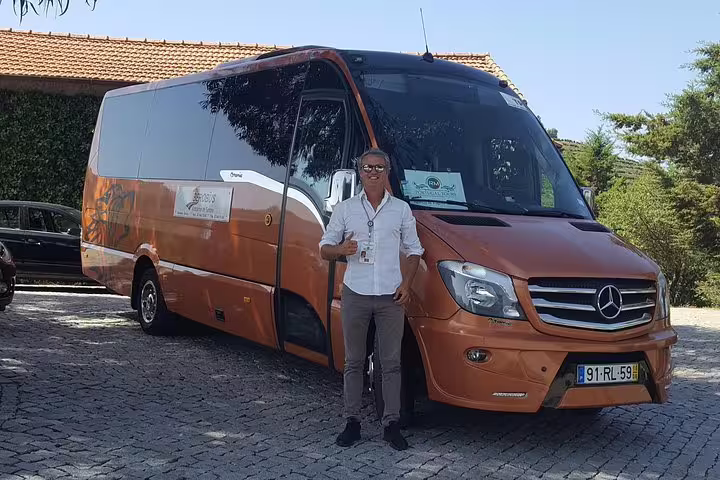 Friendly driver standing beside an orange airport transfer van ready for Lisbon hotel and apartment drop-offs.