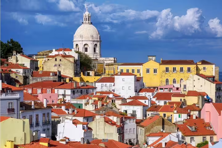 Colorful buildings with red tile roofs in Lisbon's Alfama district, with a white domed church rising above