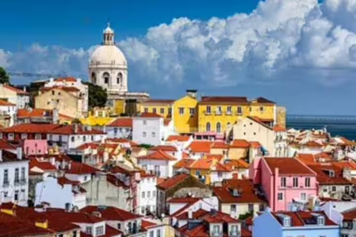 Colorful rooftops of Lisbon's Alfama district with iconic dome and ocean view, ideal for private guided tours in Portugal.