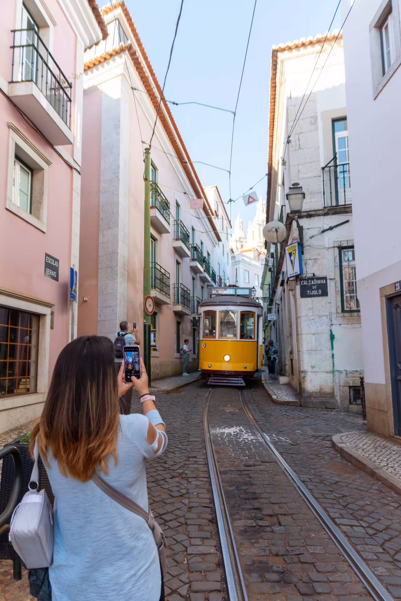 Tourist captures iconic yellow tram in Alfama's narrow cobblestone streets during a Lisbon photography tour with a local guide.