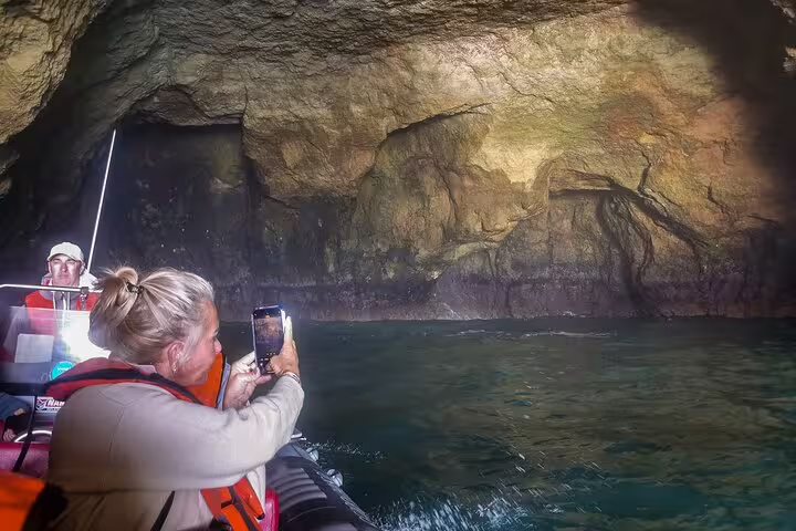 Tourists capturing stunning rock formations during a boat tour in Algarve caves on a 2-day private trip from Lisbon.