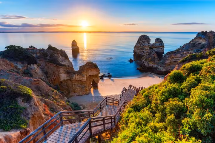 Sunset over Algarve's stunning coastline with cliffs and serene beach, highlighting the beauty of private transfers.