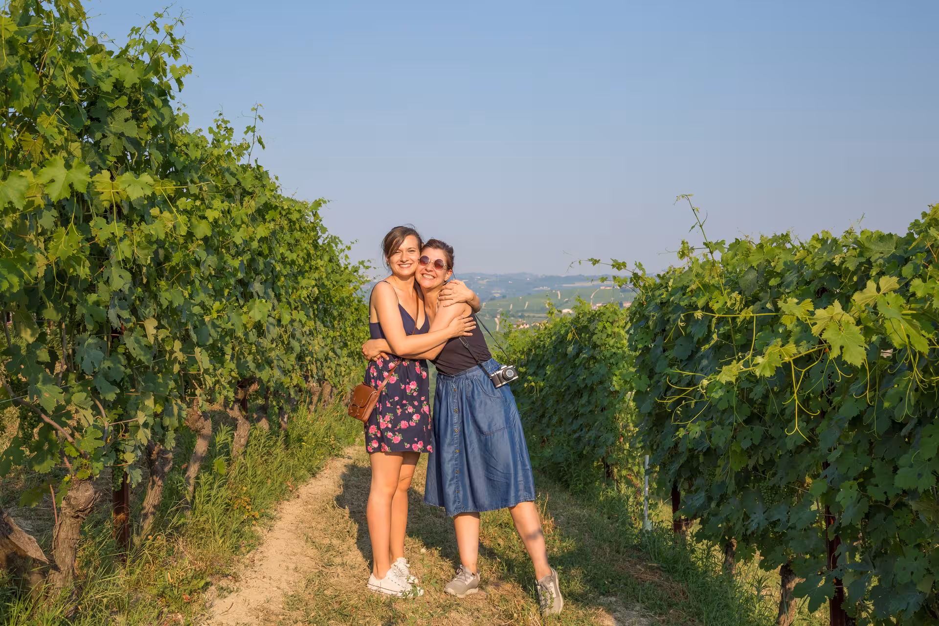 Two women smiling and hugging in a lush vineyard in Arrábida, part of the Lisbon private day tour.