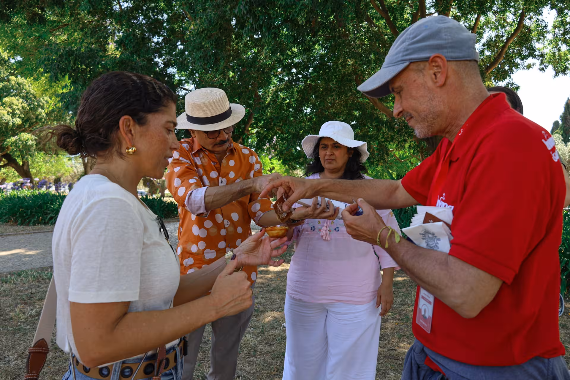 Tourists enjoy a traditional Portuguese tasting experience under lush trees in Lisbon's Belém district.