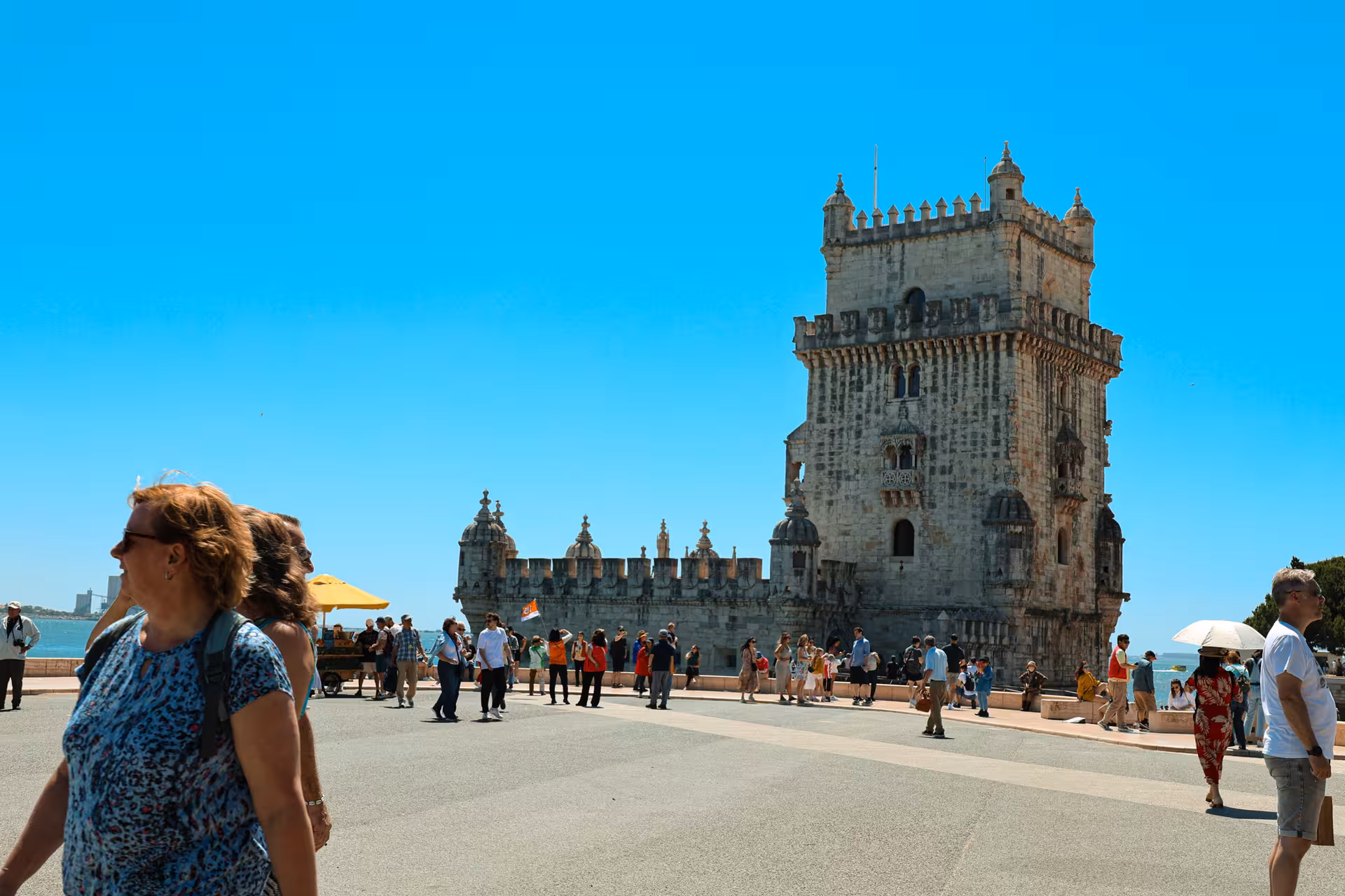 Tourists exploring the iconic Belém Tower, a highlight on the Lisbon half-day city tour, under a bright blue sky.