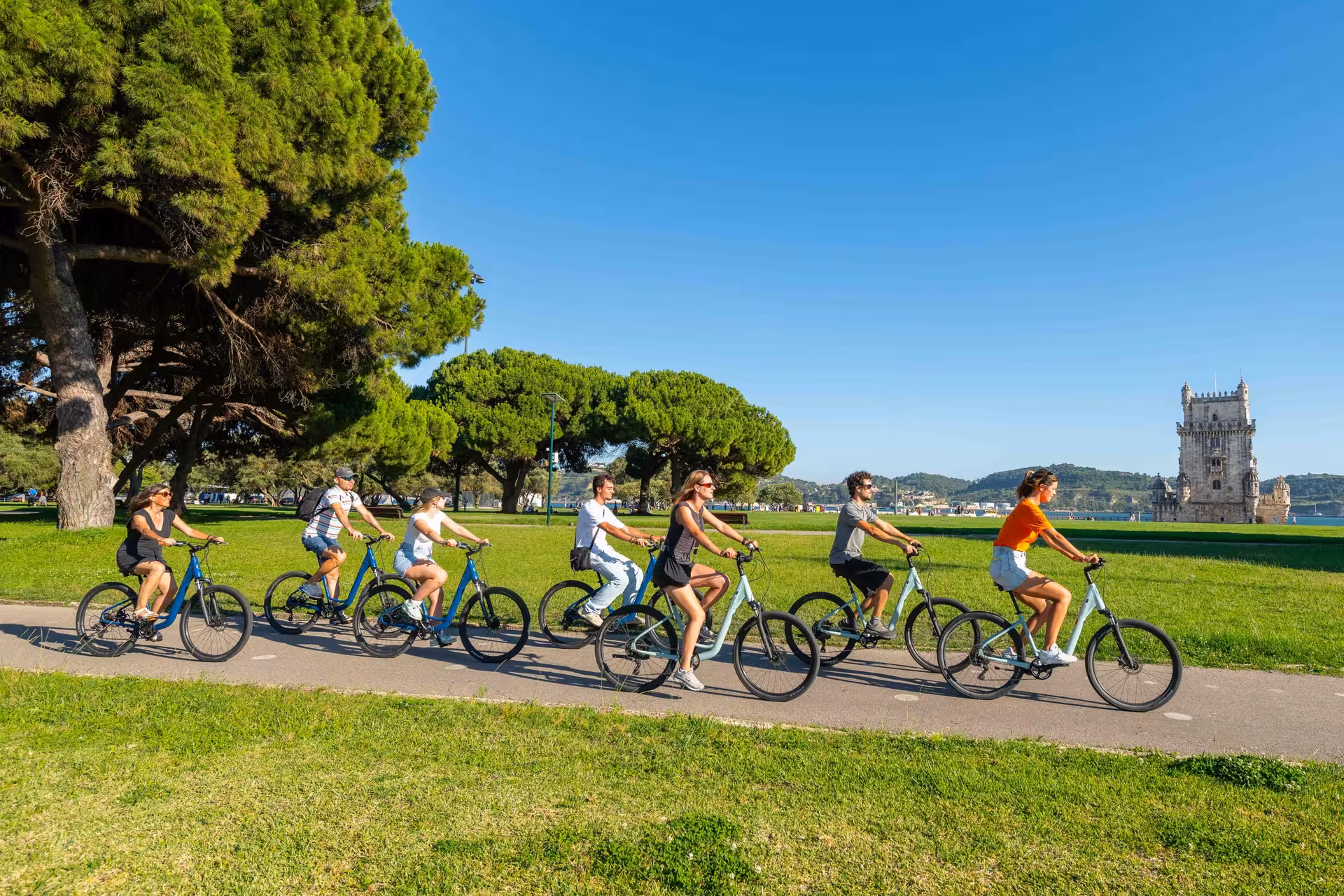 Cyclists explore scenic Lisbon paths with Belém Tower in the background on a sunny bike tour.