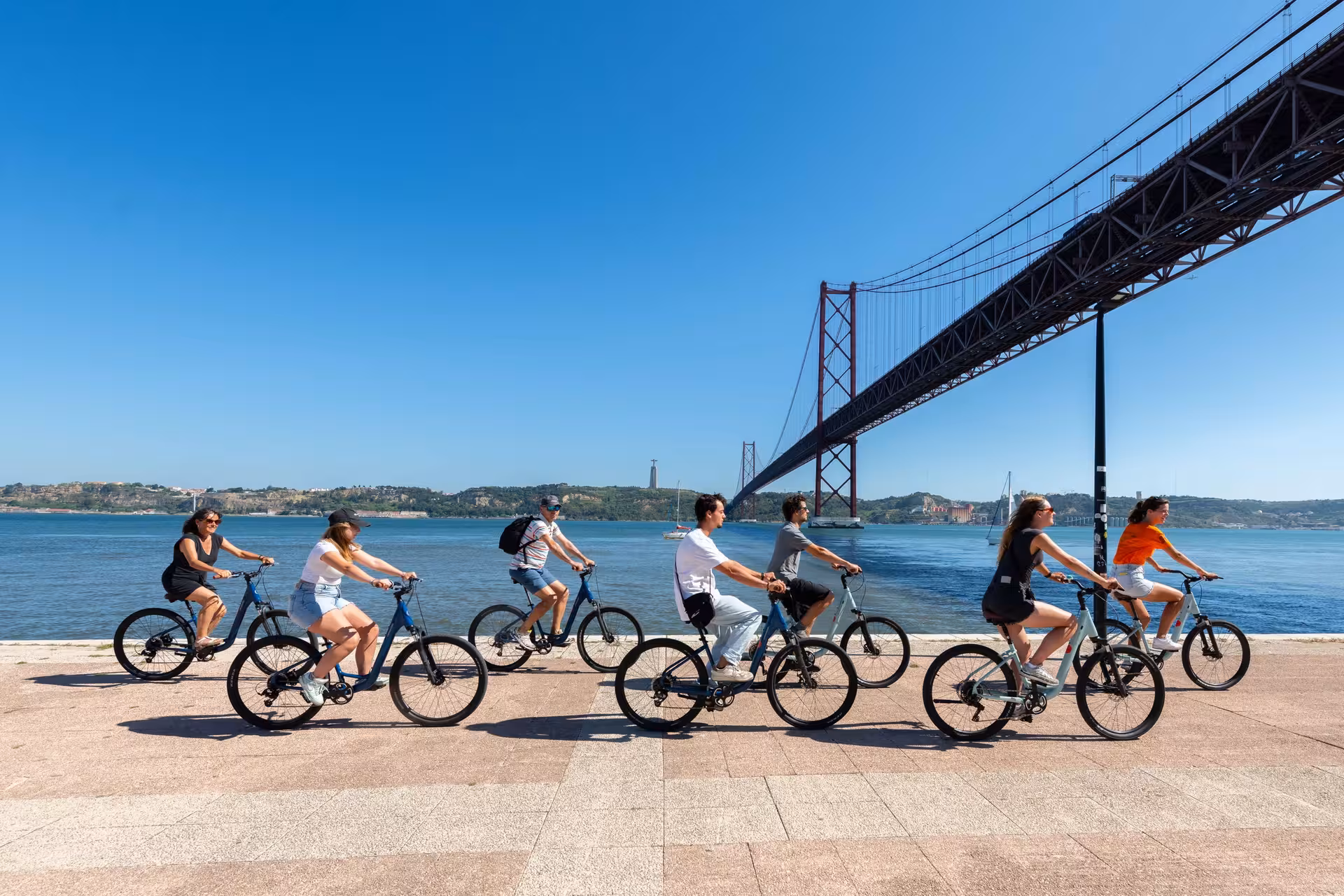 Cyclists enjoying a scenic Lisbon bike tour along the waterfront near the iconic 25 de Abril Bridge.