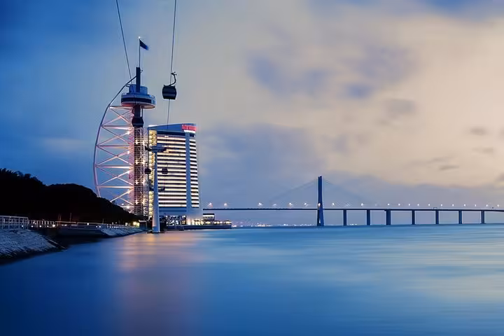 Scenic view of Lisbon's cable cars and Vasco da Gama Bridge at dusk, highlighting modern architecture and serene waters.
