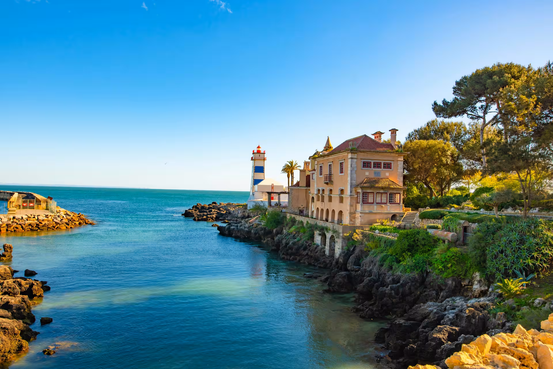 Scenic view of the coastline at Cascais with a picturesque lighthouse and historic building, perfect for Lisbon day tours.