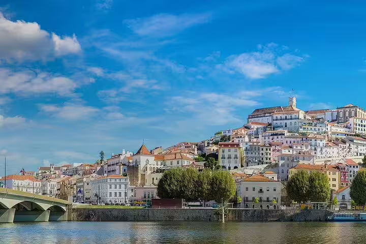 Scenic view of Coimbra's historic skyline along Mondego River, showcasing iconic architecture on a Lisbon to Coimbra private journey.
